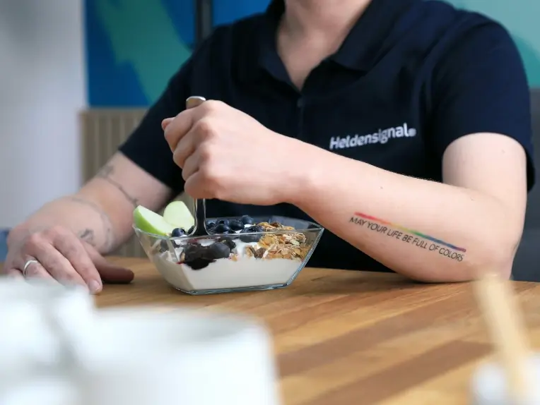 Teresa in der Mittagspause, wie sie Müsli mit Obst und Skyr isst und ein Heldensignal®-Poloshirt trägt.